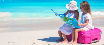Little cute girls with big suitcase and a map on tropical beach
